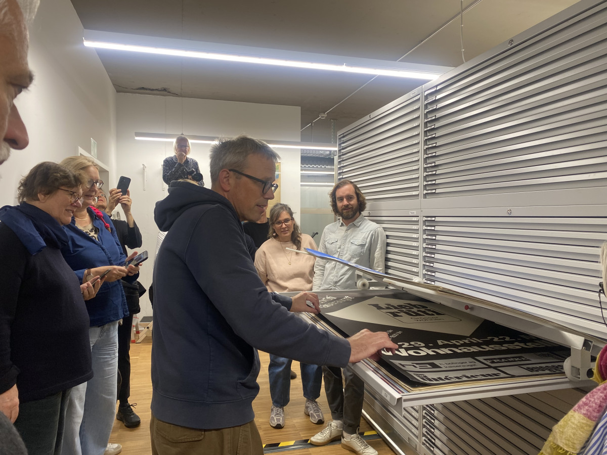 Gruppenführung im Archivraum, eine Person zieht ein großformatiges Plakat aus einer flachen Schublade.