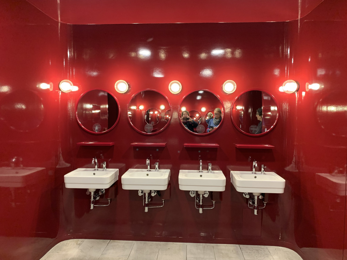 Roter Waschraum mit weißen Waschbecken und runden Spiegeln.
