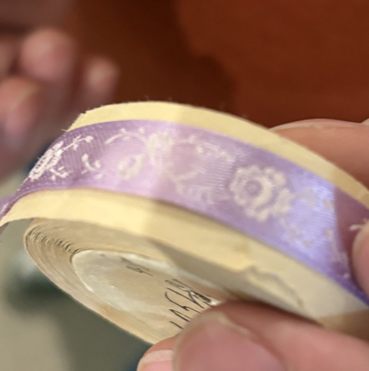 Nahaufnahme einer Hand, die eine Rolle mit lilafarbenem Band mit floralen Mustern hält.