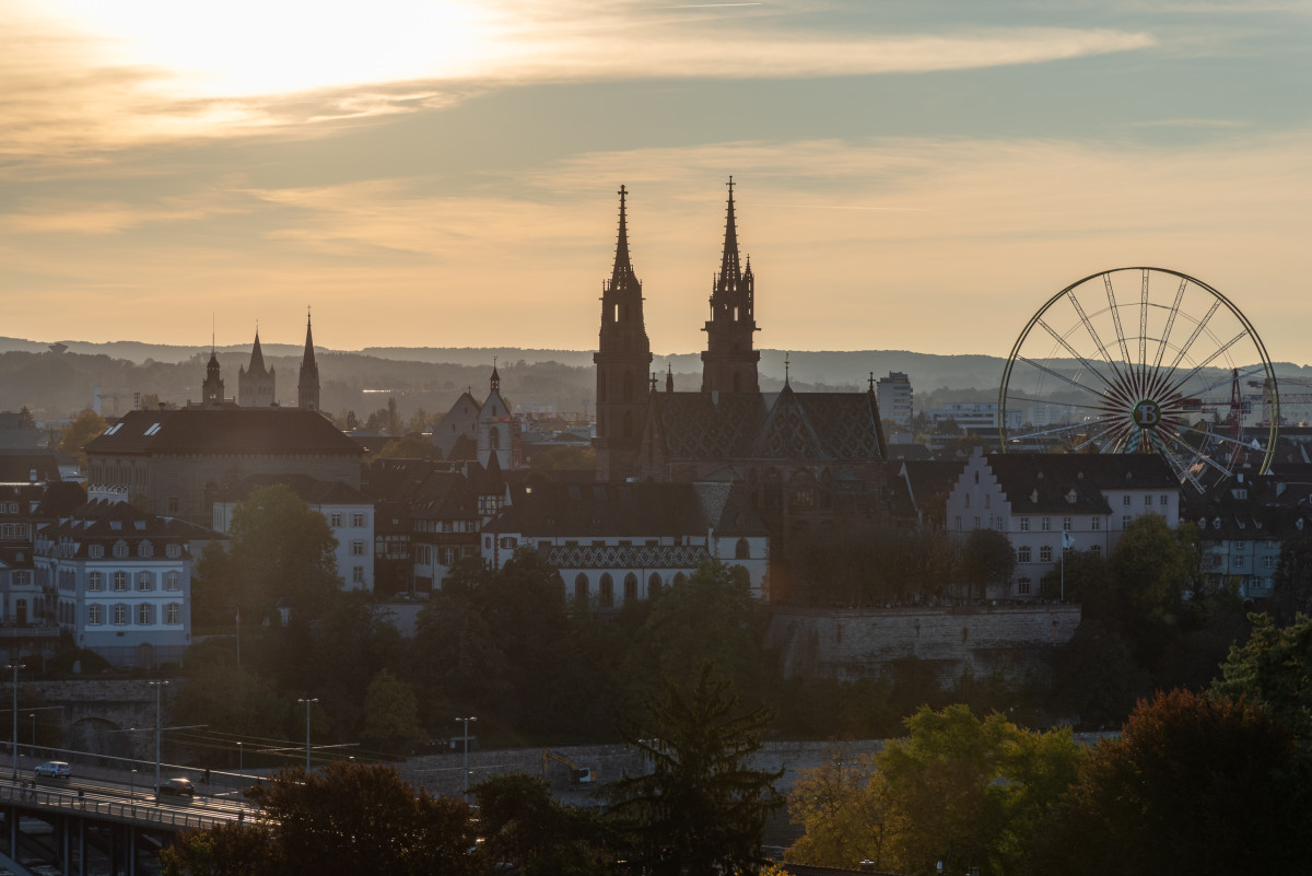 Panorama von Basel bei Sonnenuntergang mit Münster, Altstadt und Riesenrad im Hintergrund.