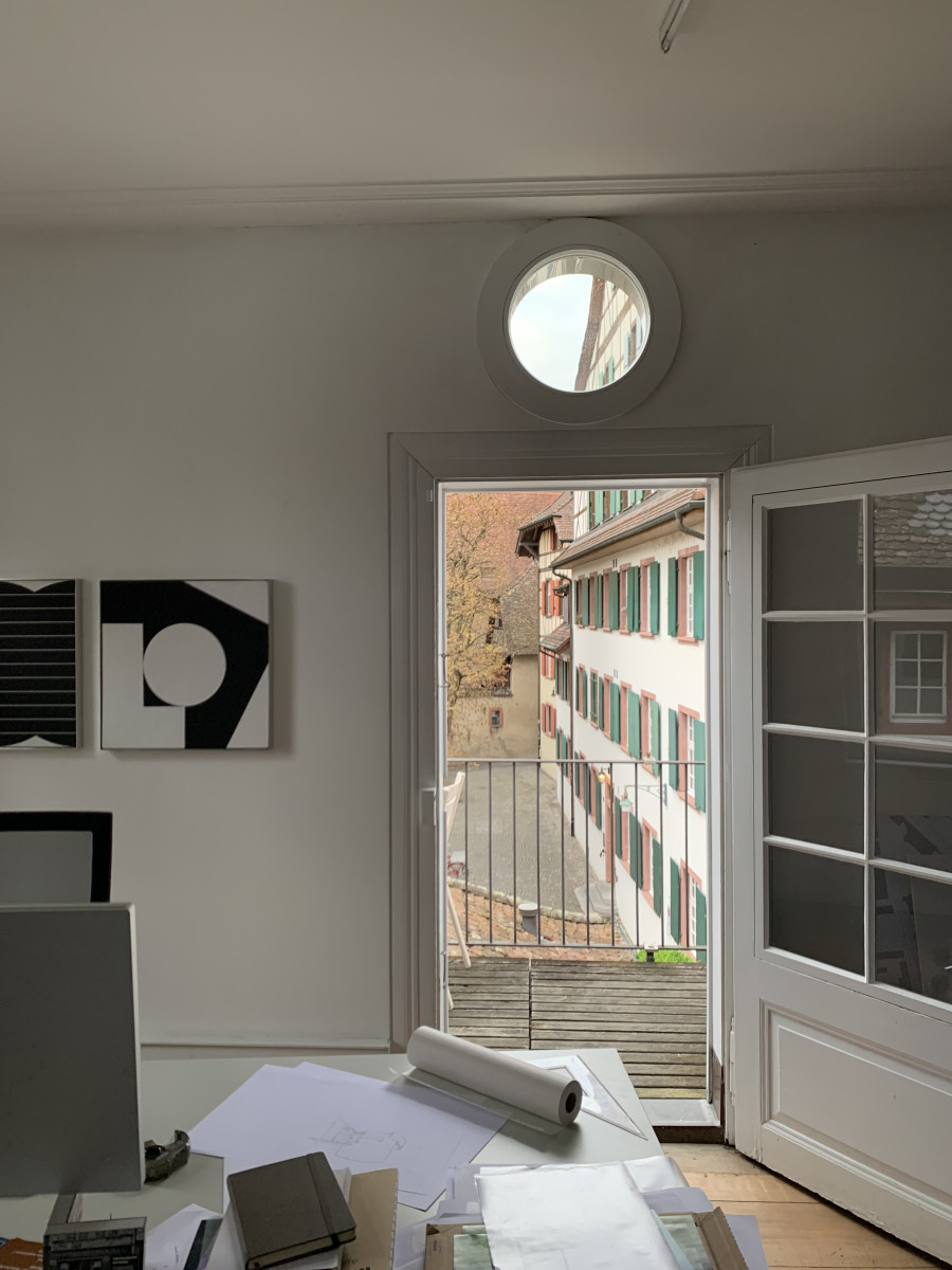 Blick aus einem Büro auf eine Gasse mit alten Häusern, durch eine geöffnete Tür mit Rundfenster.