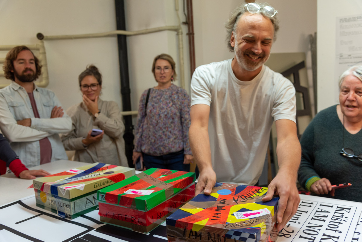 Jiri Oplatek zeigt bunt beklaebte Kartons, umgeben von einer kleinen Gruppe, die aufmerksam zuschaut.