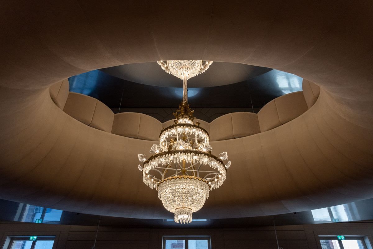 Prunkvoller Kronleuchter hängt unter einer abgerundeten Decke.