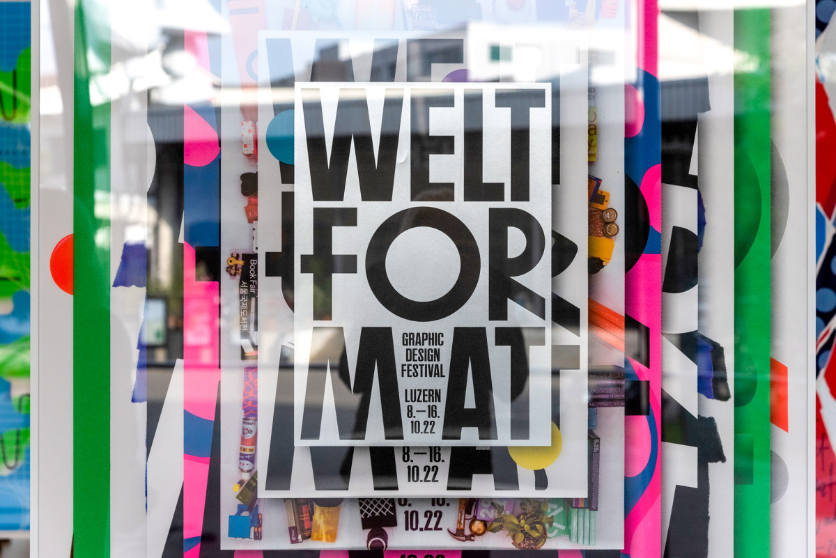 Plakat mit der Aufschrift „Weltformat – Graphic Design Festival Luzern“ in einer farbenfrohen Ausstellung.