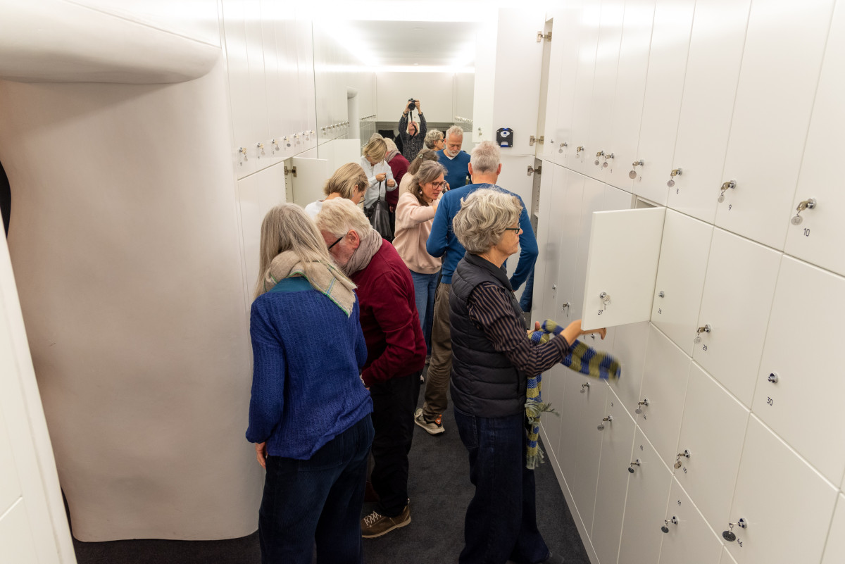 Gruppe von Besucherinnen und Besuchern verstaut ihre Sachen in weißen Schließfächern.