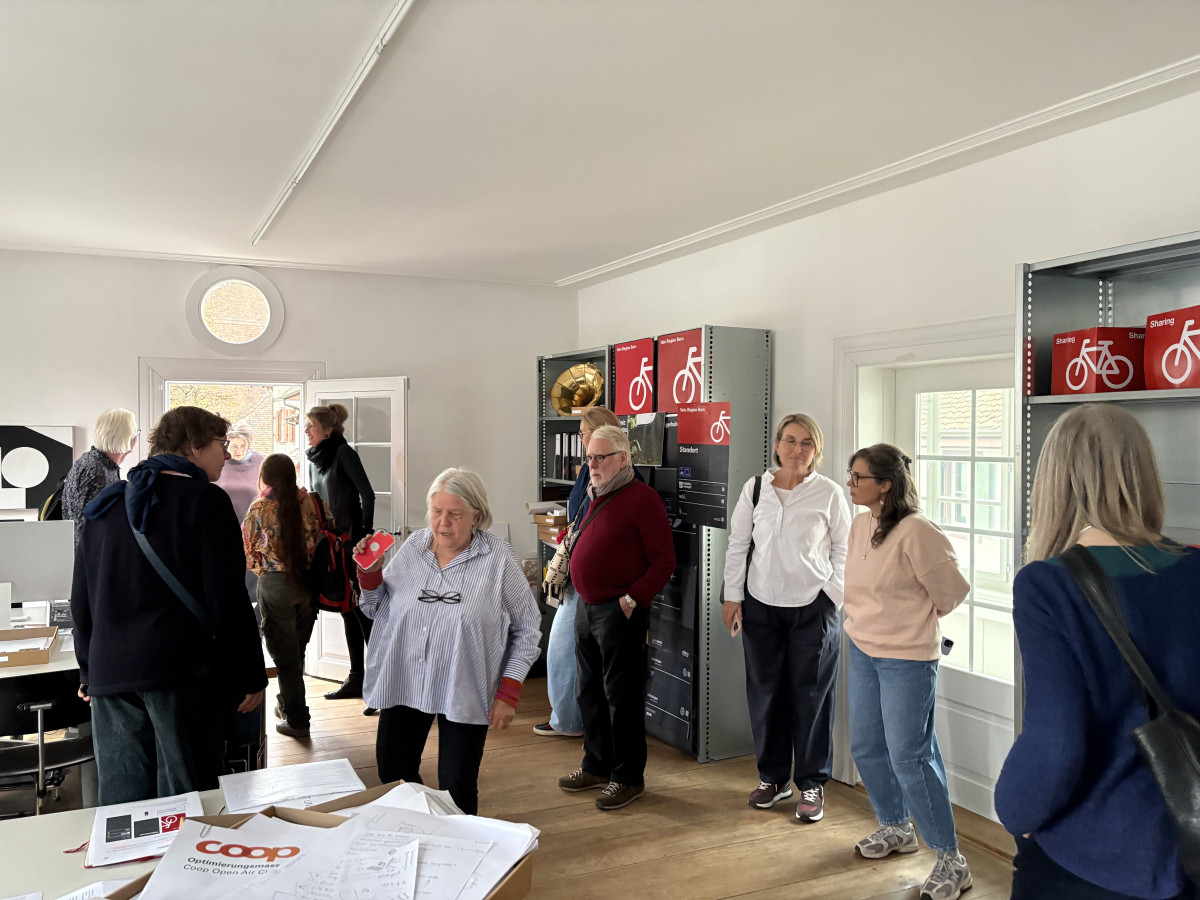 Reisegruppe steht und unterhält sich in einem hellen Büro mit Regalen und Plakaten an der Wand.