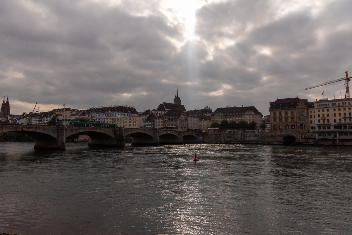 Blick auf die Mittlere Brücke in Basel, mit historischen Gebäuden am Rheinufer unter bedecktem Himmel.