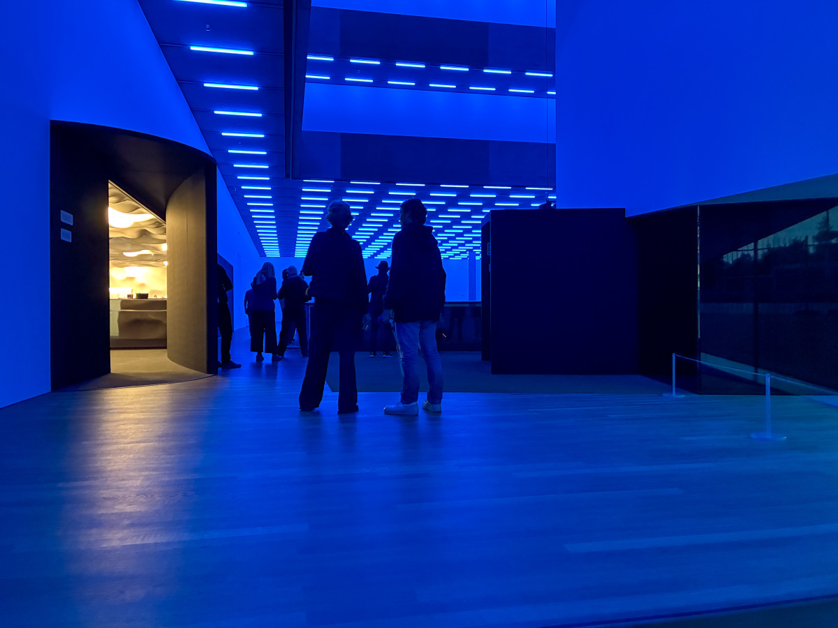 Innenraum mit blauer Lichtinstallation, Menschen stehen und unterhalten sich im futuristisch beleuchteten Raum.
