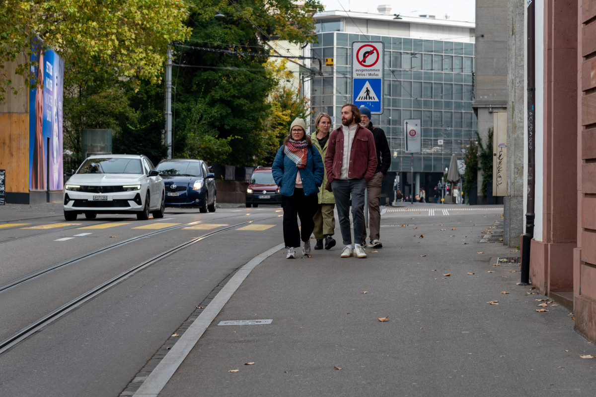 Gruppe von Menschen spaziert auf einer Basler Straße entlang der Tramgleise.