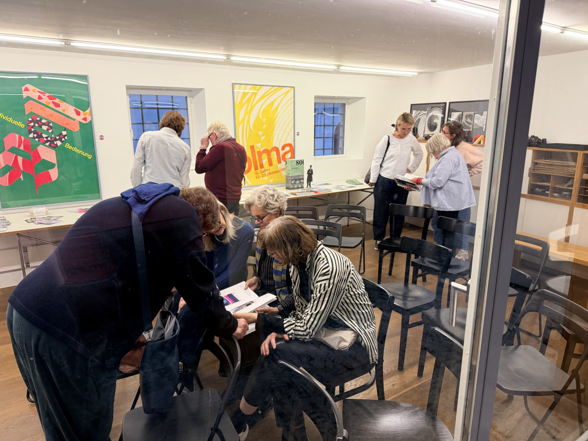 Besuchergruppe betrachtet Bücher und Plakate in einem hellen Ausstellungsraum.