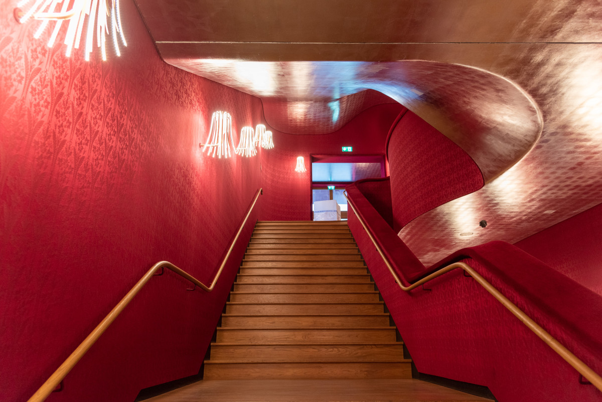 Treppenaufgang mit roten Wänden und dekorativer Beleuchtung in einem Theater oder Museum.