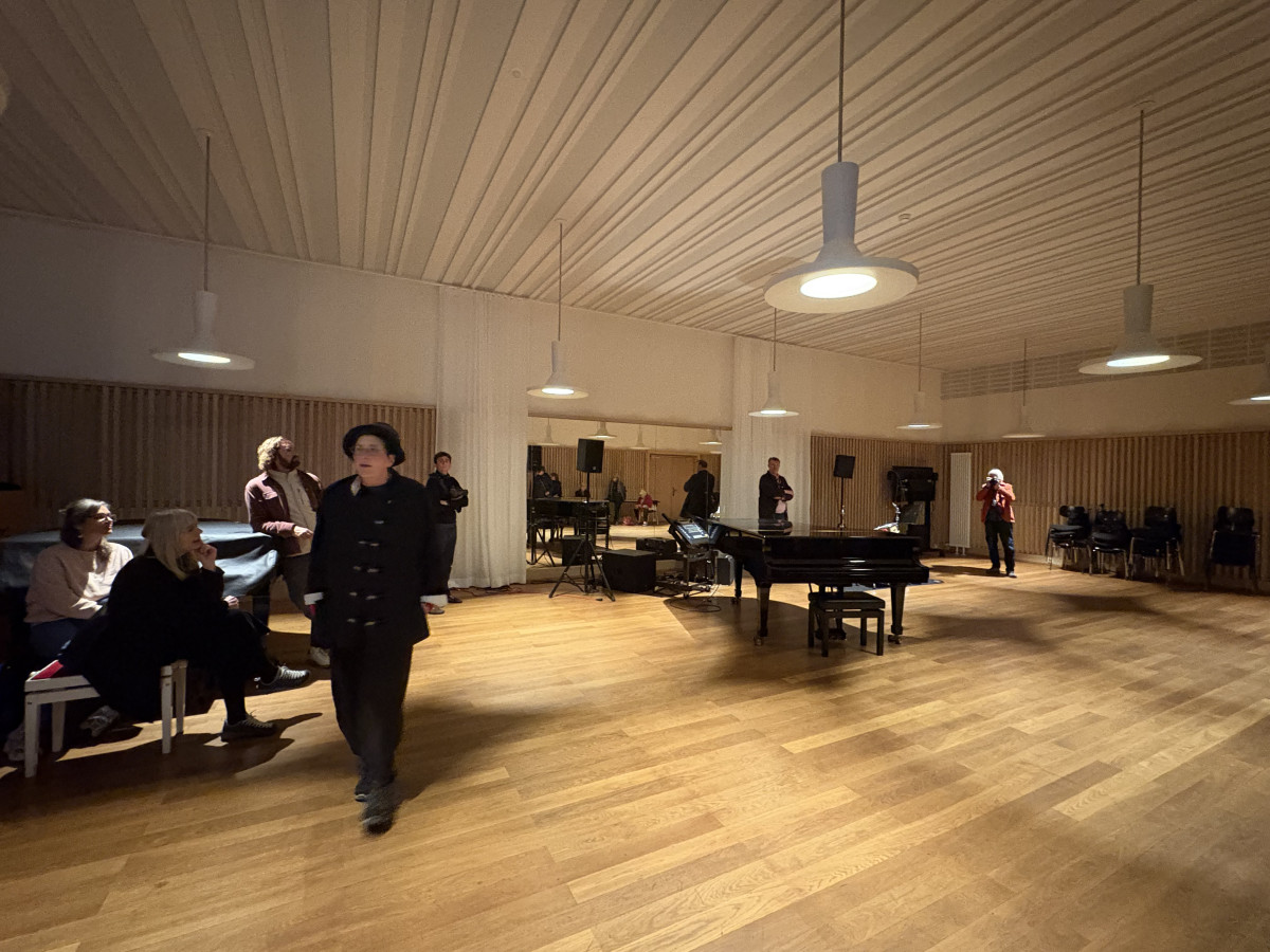 Personen in einem großen Raum mit Flügel und Holzfußboden, stimmungsvolle Beleuchtung.