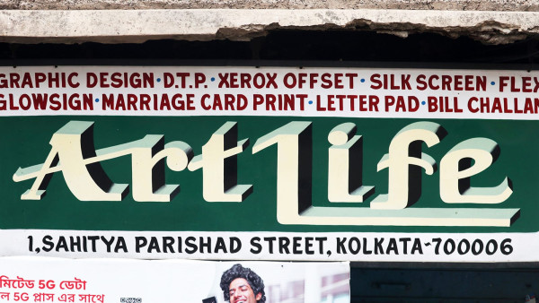 Ein bemaltes Schild für einen DTP-Shop namens „ArtLife“. Der Name ist in Weiß auf grünem Hintergrund geschrieben, und eine Liste der angebotenen Dienstleistungen ist in Rot auf Weiß geschrieben.