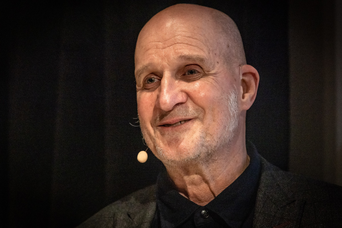 Das Bild zeigt eine Nahaufnahme von Ulysses Voelker, ein älterer, glatzköpfiger Mann mit einem leichten Bart. Er trägt ein dunkles Hemd und darüber ein Sakko.